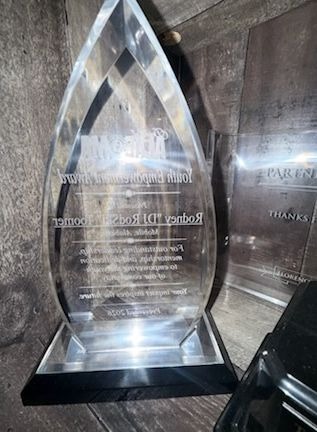 A clear teardrop-shaped crystal award on a black base, engraved and presented to Rodney Toomer